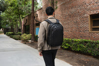 Man walking outdoors with a black backpack near a brick building