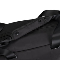 Close-up of a black duffel bag showing a wide shoulder strap with metal snap buttons, a zipper, and black webbing straps on a white background.