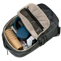 Open backpack with items including a blue mug, white device, and books on a black background