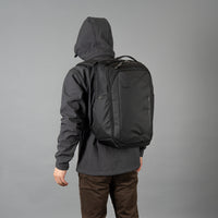 Person wearing a black backpack with a gray background