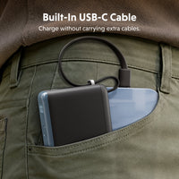 A black portable power bank with a built-in USB-C cable tucked into the back pocket of olive green pants, next to a light blue smartphone. White text at the top reads 'Built-In USB-C Cable' and 'Charge without carrying extra cables.