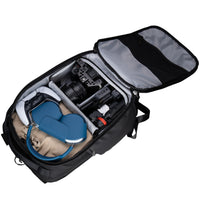 Open black laptop backpack with camera equipment and blue shoes on a white background