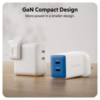 Two compact GaN chargers on a wooden surface with a soft blurred background. One charger is shown from the back in white, and the other is shown from the side in white with a blue front panel featuring two USB-C ports.