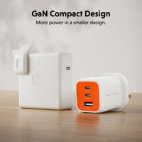 Two compact wall chargers on a wooden surface against a soft light background. One charger is matte white with an embossed Apple logo, and the other is white with a bright orange front panel featuring three USB-A ports and one USB-C port.