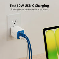 A white and blue USB-C power adapter plugged into a wall outlet, with two blue and white cables connected. Text at the top reads 'Fast 60W USB-C Charging' and a tablet is partially visible on the right.