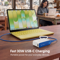 A portable white and blue USB-C power bank connected to a yellow laptop on a wooden table, with a woman working at a cafe in the background. Text overlay reads 'Fast 30W USB-C Charging Portable power for your everyday devices.